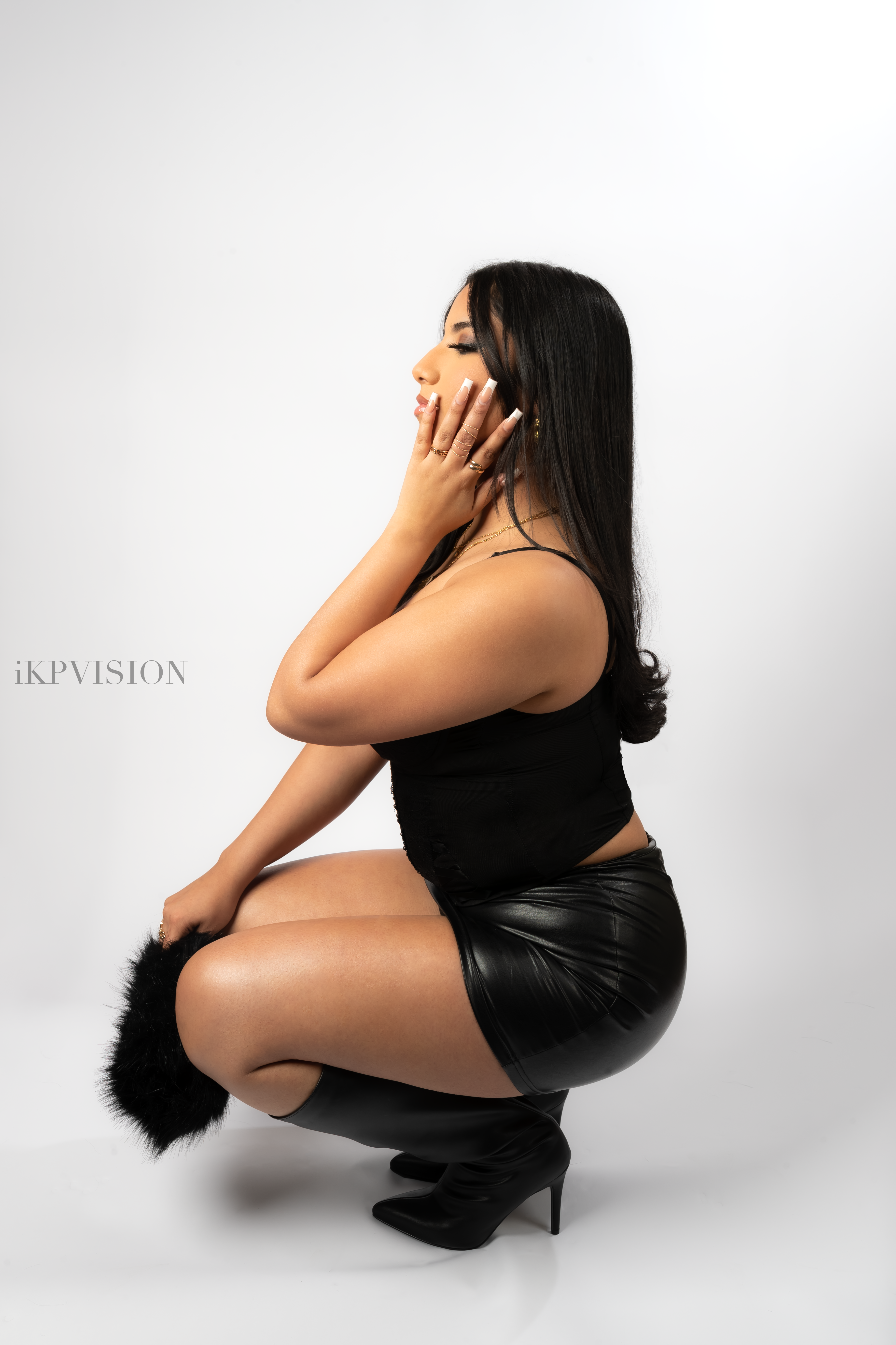 Studio portrait of a woman crouching in profile in a black outfit against a white background, with an IKPVISION watermark.