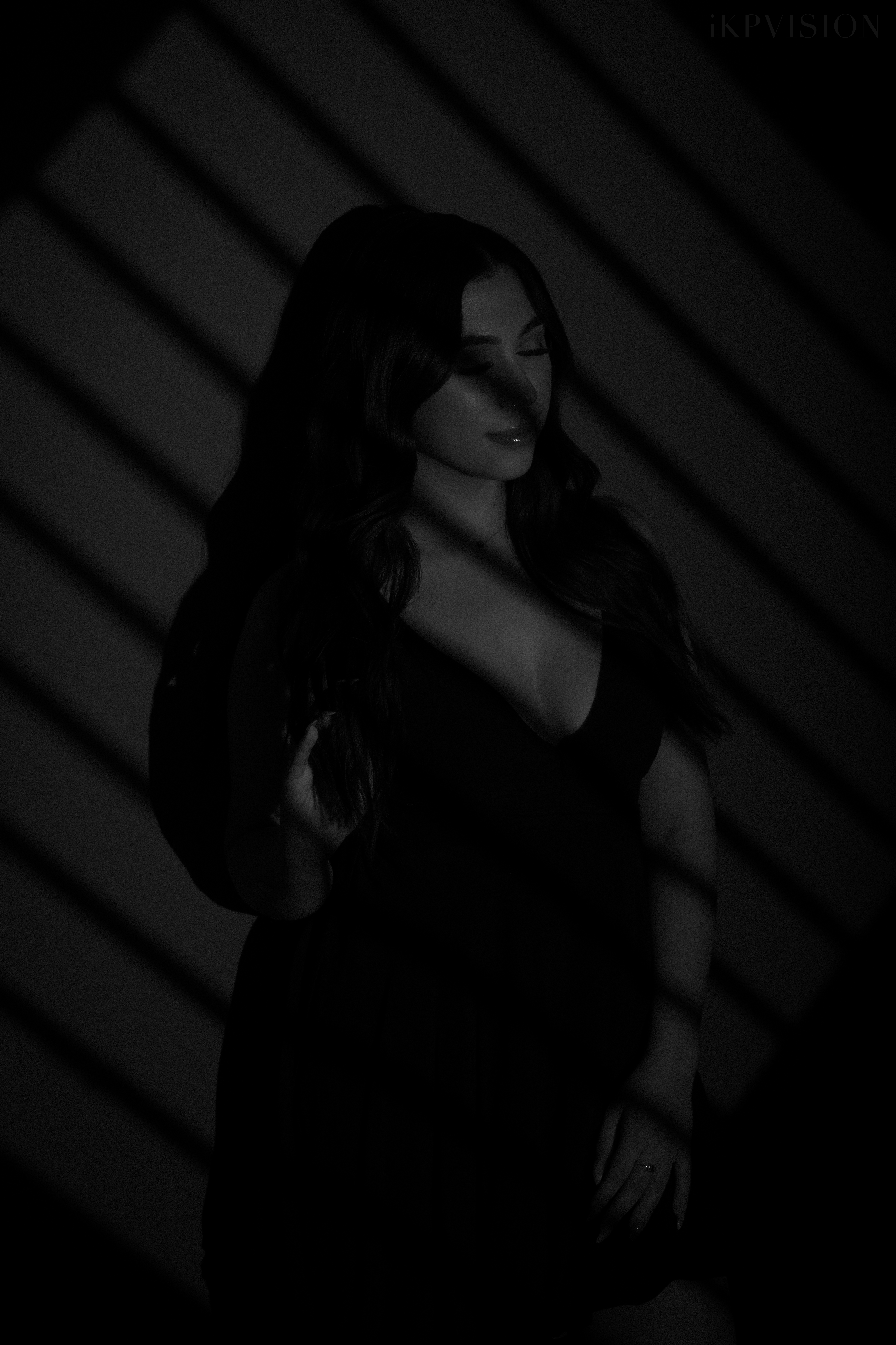Black-and-white portrait of a woman in a black dress, framed by diagonal shadows, with an IKPVISION watermark.